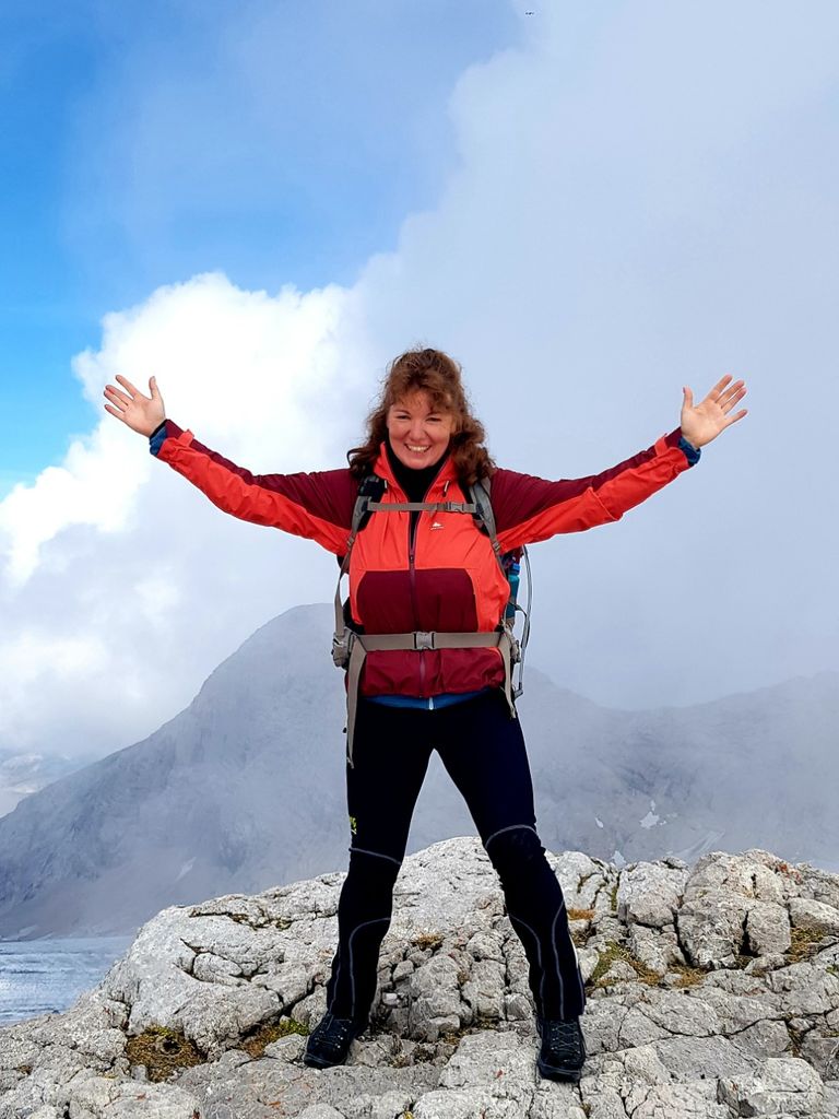 Lächelnde Frau auf einem Berggipfel. Voller Stolz und Lebensfreude reißt sie die Arme nach oben